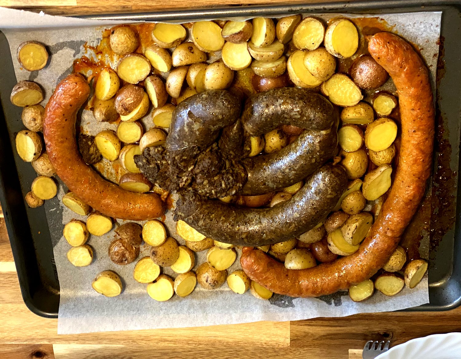 Kolbász and hurka roasting on a sheet pan with halved baby potatoes