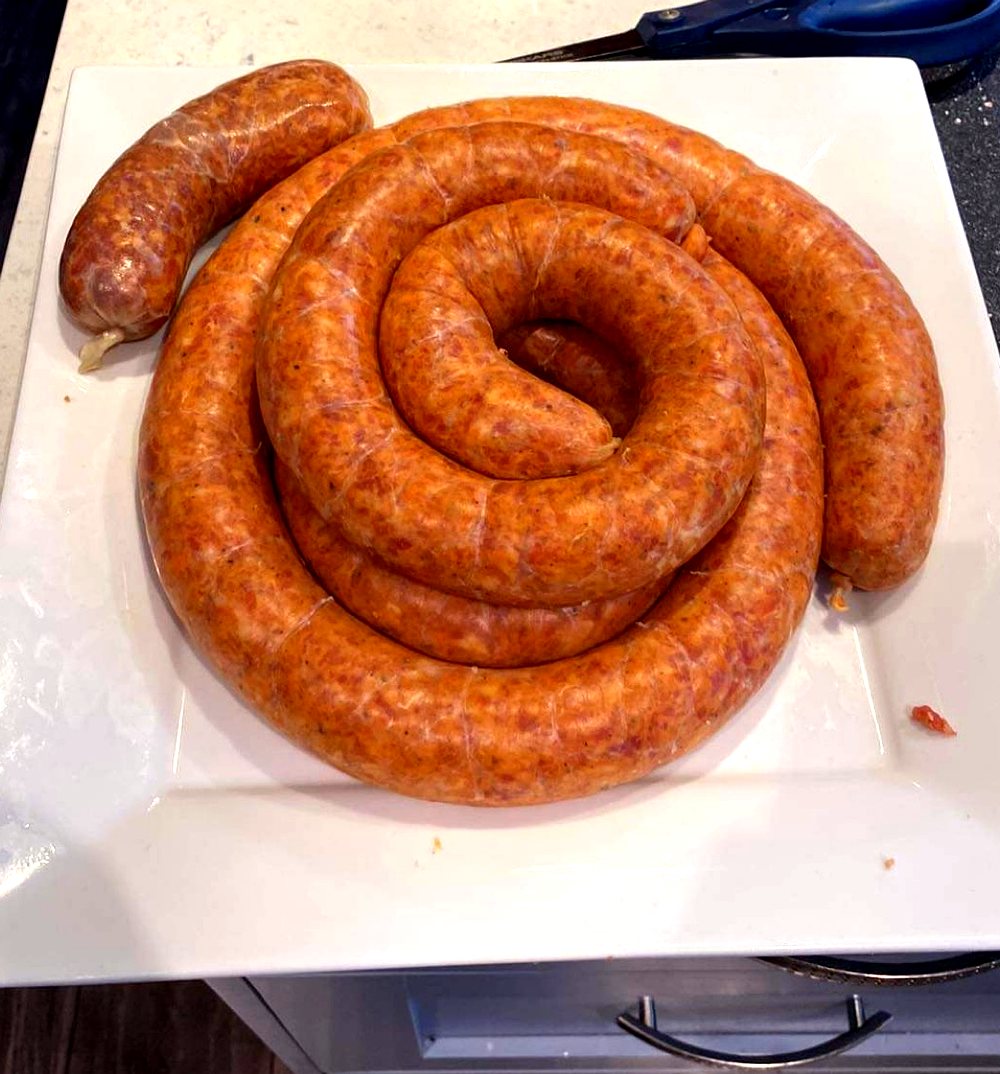 A freshly hand-stuffed coil of Hungry Dane paprikás kolbász on a white plate, ready to cook